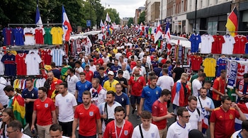Calle con puestos de venta y gran multitud de personas que caminan. Se observan banderas y camisetas de selecciones de fútbol.