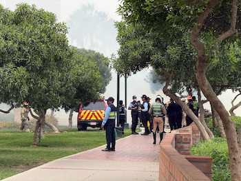 Varios agentes de policía y de seguridad permanecen en una acera junto a un vehículo de emergencia y árboles rodeados de humo