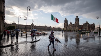 Personas caminan con sombrillas sobre el pavimento mojado en la plaza del Zócalo, frente a la Catedral Metropolitana de la Ciudad de México.