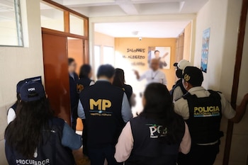 Vista trasera de personal del Ministerio Público, Policía Nacional Civil y PDH con chalecos y gorra, caminando en un pasillo de una institución educativa