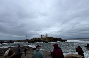 En esta foto tomada con un teléfono inteligente, unas personas observan las olas en el faro Nubble de York, Maine, durante una tormenta del noreste, el sábado 26 de septiembre de 2026 (AP /Caleb Jones)