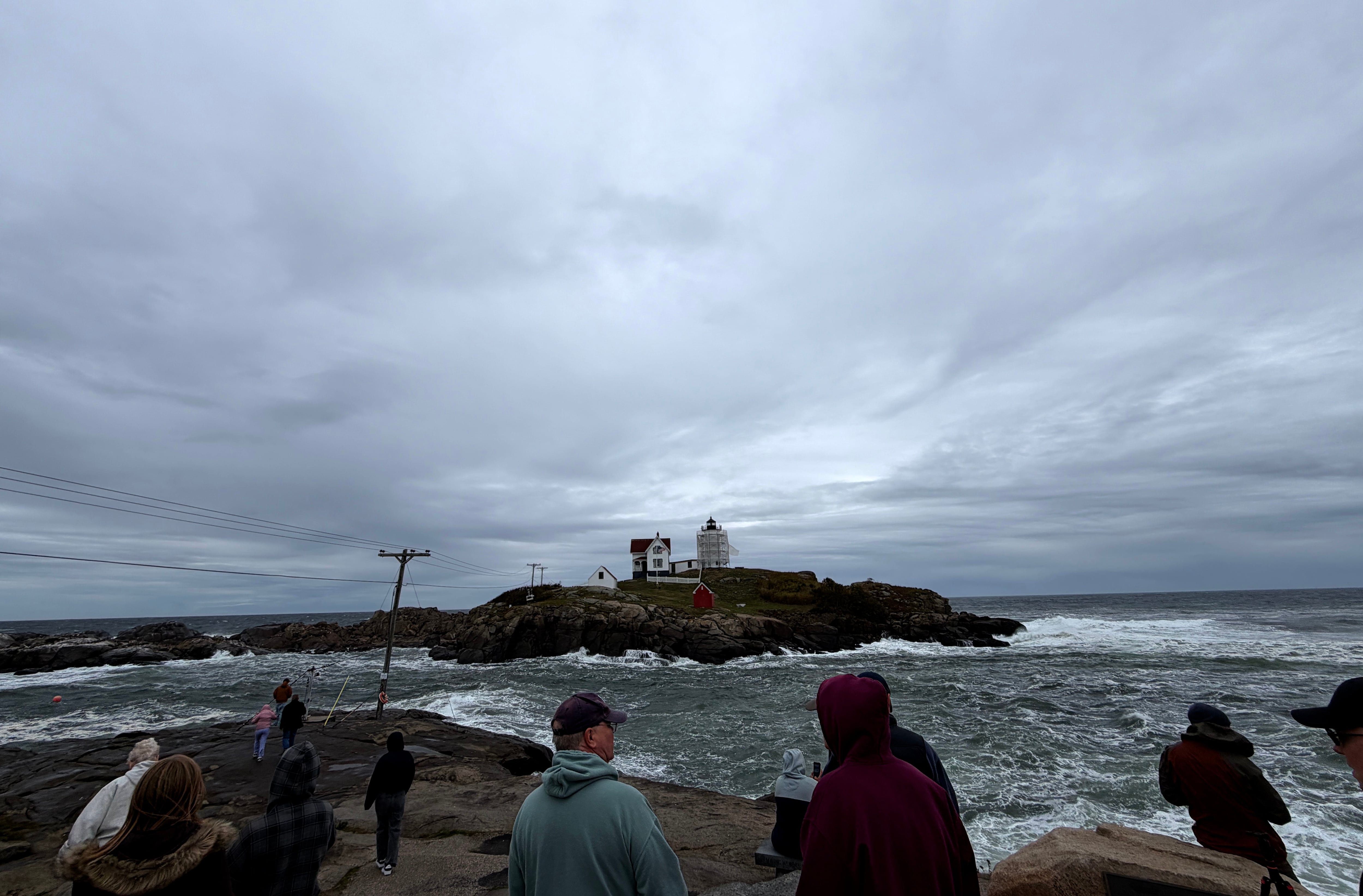 En esta foto tomada con un teléfono inteligente, unas personas observan las olas en el faro Nubble de York, Maine, durante una tormenta del noreste, el sábado 26 de septiembre de 2026 (AP /Caleb Jones)