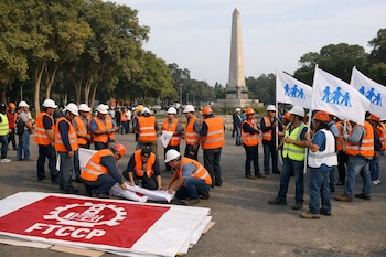 Um grupo de pessoas com roupas refletivas e capacetes coloca faixas da FTCCP e bandeiras da EsSalud em frente a obeliscos, árvores e asfalto.