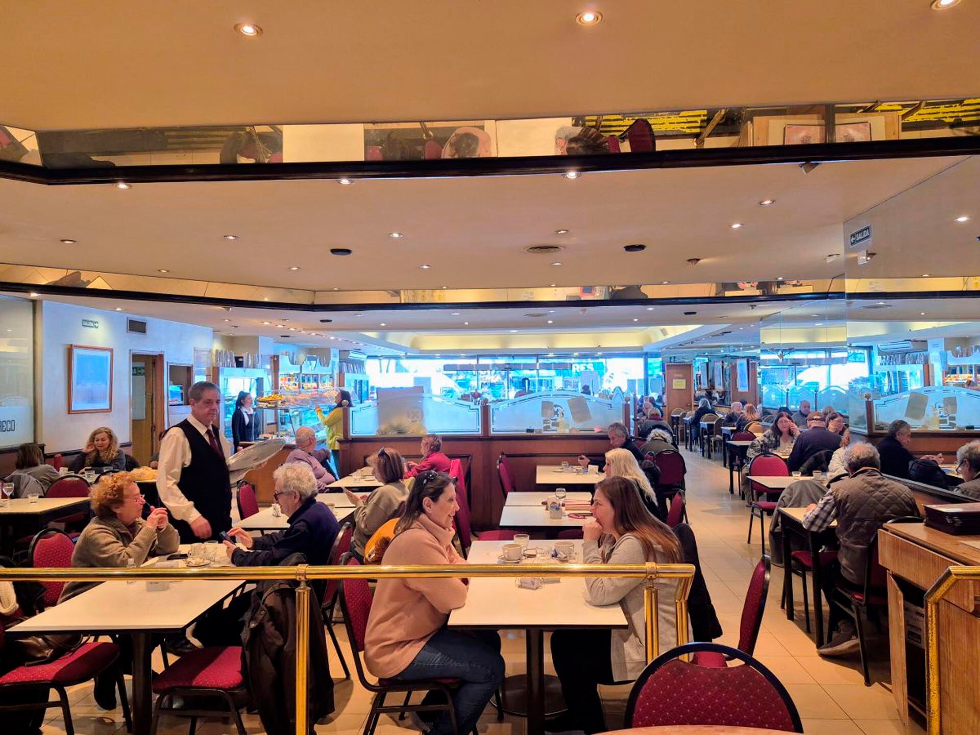 Hoy El Greco es una confitería elegante con un gran salón, una isla en el centro donde se exhiben productos de pastelería y sillas tapizadas color rojo oscuro