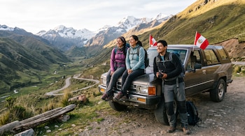 Tres personas con mochilas junto a un vehículo gris con dos banderas peruanas. Fondo de montañas nevadas, un valle verde y una carretera sinuosa.