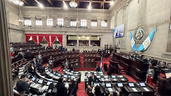Vista aérea de un amplio hemiciclo con asientos escalonados de tela roja. Presencia de personas, incluyendo personal uniformado, banderas y un escudo nacional