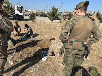 Un grupo de militares con uniformes de camuflaje trabaja en el suelo con estructuras metálicas cerca de vehículos militares al aire libre