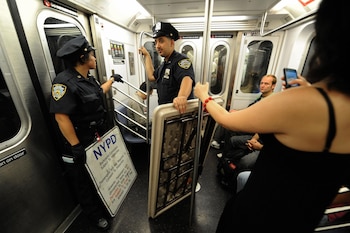 Oficiales del NYPD inspeccionan el interior de un tren mientras interactúan con pasajeros, como parte de los operativos de seguridad en el sistema de transporte.