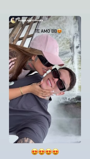 Tamara Báez, con gorra rosa y gafas, besa la mejilla de su pareja, Thiago Martínez, quien sonríe con gafas, frente a las Cataratas del Iguazú