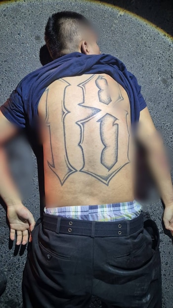Vista posterior de una persona con camiseta azul, pantalones oscuros, calzoncillos de cuadros y un tatuaje grande en la espalda