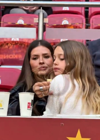China Suárez, con cabello oscuro y chaqueta negra, sostiene comida para su hija Magnolia, de cabello largo y claro, vestida con suéter blanco, en un estadio