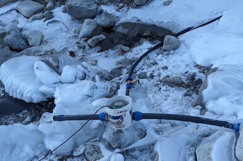 Tuberías de plástico negro conectadas a un balde blanco con cables sobre rocas con hielo y nieve