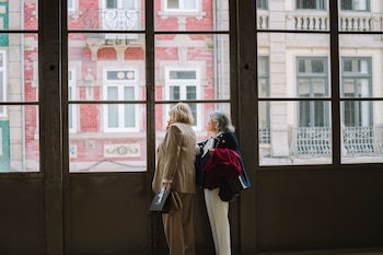 Dos mujeres mayores miran a través de una ventana (Canva)