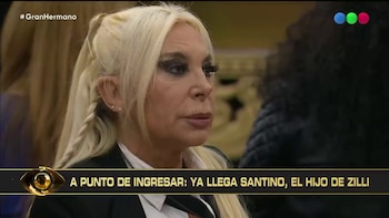 Mujer rubia de cabello largo y trenzado, con maquillaje oscuro. Banner inferior con texto blanco "YA LLEGA SANTINO, EL HIJO DE ZILLI" y ojo dorado. Logo Gran Hermano
