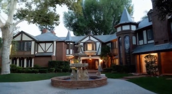 Mansión Tudor de ladrillo rojo y blanco, con tejados oscuros y torrecillas. Frente a la entrada, una fuente ornamental de piedra con agua fluyendo