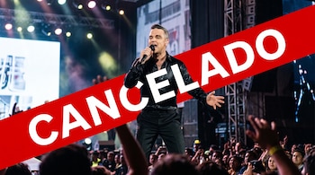 Robbie Williams canta sobre un escenario frente al público con una franja roja transversal que dice CANCELADO.