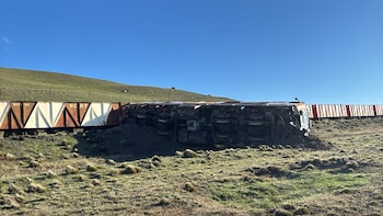Una locomotora y vagones de un tren de carga volcados sobre un campo de hierba junto a una colina bajo un cielo despejado