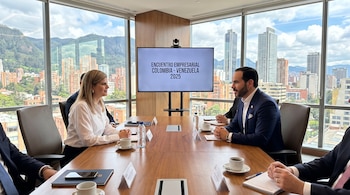 Personas sentadas a la mesa en una oficina con un televisor que presenta el texto Encuentro Empresarial Colombia