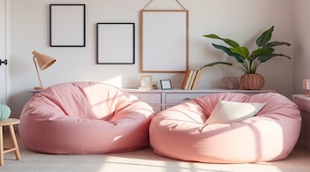 Dos sillones puf rosados sobre una alfombra clara en un salón con cuadros en la pared, un mueble, una lámpara y una planta.