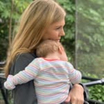 Maren Morris, una mujer rubia, sostiene a una niña pequeña de espaldas con un mono a rayas de colores, mirando hacia la derecha