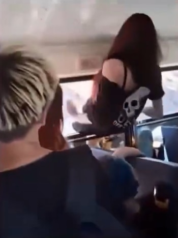 Una persona vestida de negro se introduce por la ventana de un autobús frente a jóvenes sentados en los asientos