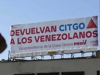 Una valla publicitaria blanca con el mensaje "DEVUELVAN CITGO A LOS VENEZOLANOS" en letras rojas y azules, y el logo del PSUV, bajo un cielo azul claro