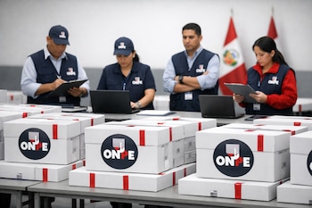 Cuatro funcionarios de la ONPE con chalecos azules y rojos custodian cajas blancas de votos selladas, apiladas sobre mesas en una sala institucional. Banderas de Perú al fondo.