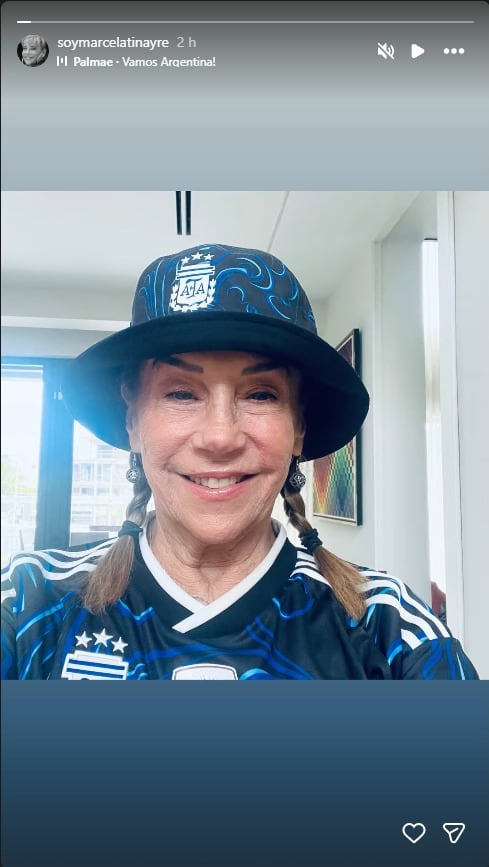 Marcela Tineyre sonríe mientras posa con la camiseta y un sombrero de la selección argentina de fútbol en un interior.