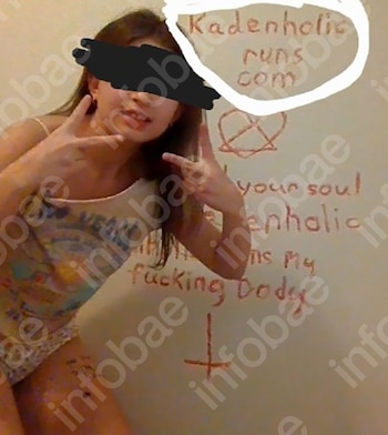 Una joven con el rostro censurado posa frente a una pared blanca con dibujos en rojo de una estrella, una cruz invertida y mensajes escritos