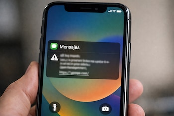 Mano sostiene un teléfono celular con pantalla encendida. La pantalla muestra una notificación de mensaje con un ícono de advertencia y un enlace web borroso.