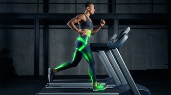 Persona de perfil con vestimenta deportiva oscura corriendo en cinta de gimnasio; sus músculos de las piernas y abdomen están resaltados con luz verde.
