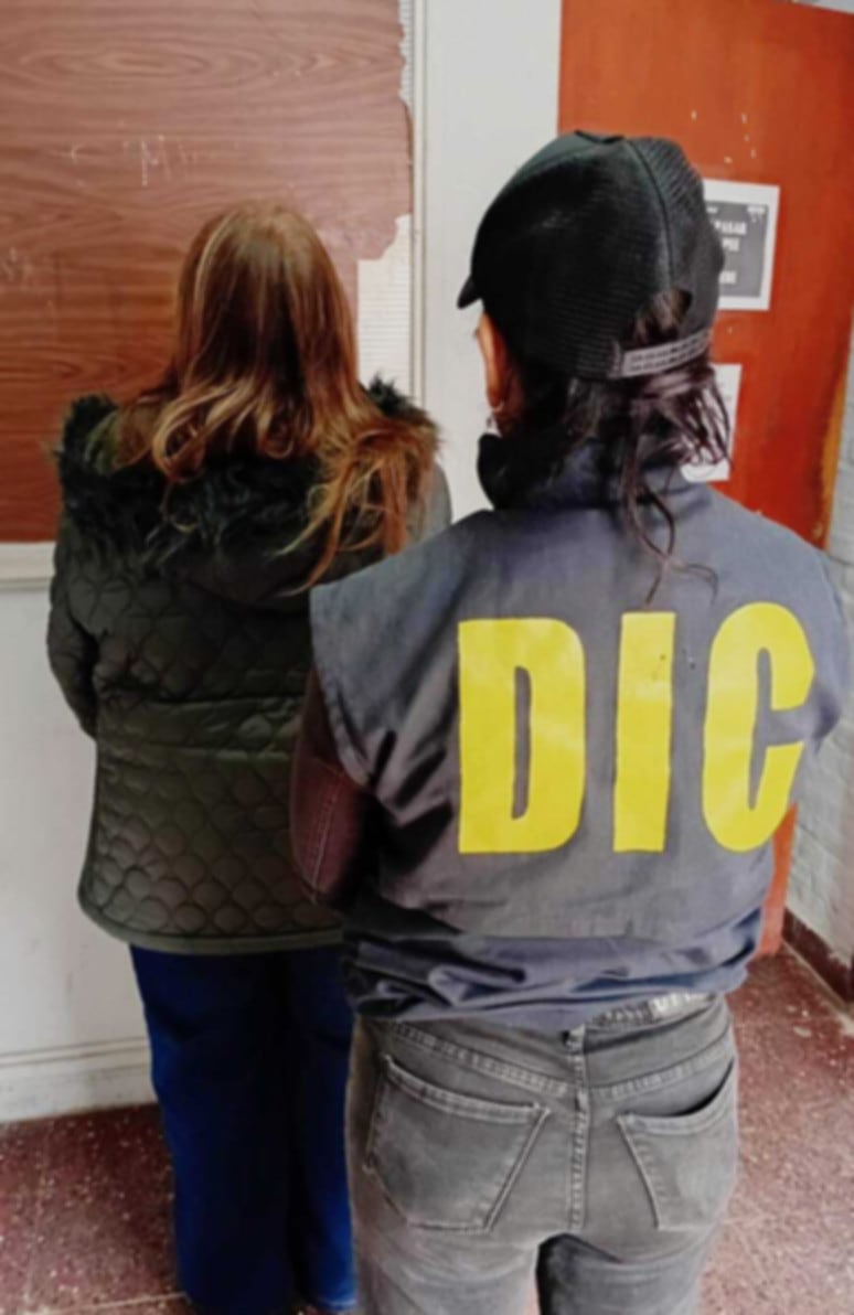 Una mujer detenida se encuentra de espaldas, custodiada por un agente con chaleco del DIC, en el marco de una investigación por la muerte de un hombre en Resistencia, Chaco (Policía de Chaco)