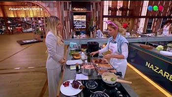 Wanda Nara vestida con traje claro habla con Karina Mazzocco, quien lleva delantal blanco y cocina en una mesada de trabajo