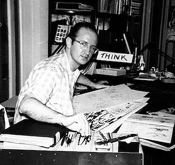 Hombre sentado en un escritorio con gafas y camisa a cuadros, dibujando en papel. Varios útiles de arte, libros y un cartel con la palabra "THINK"