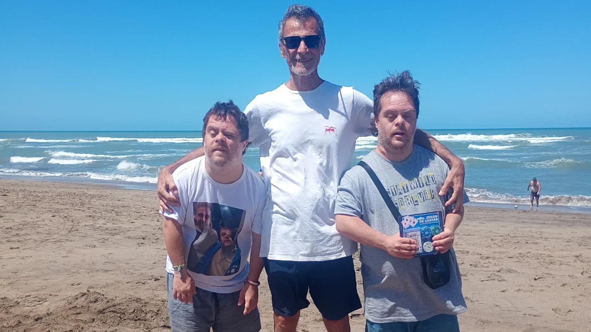 Gustavo Garzón posa sonriente junto a sus hijos en una playa de arena clara, con el mar azul de fondo bajo un cielo despejado.