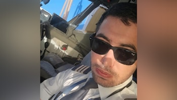 Un hombre con uniforme de piloto y gafas de sol oscuras posa dentro de la cabina de un avión