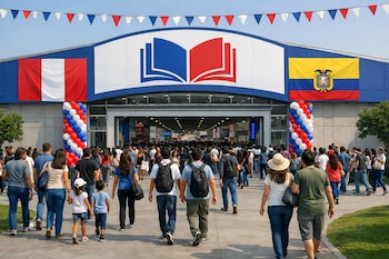 Vista general de la entrada de un edificio azul con un logo de libro abierto, banderas de Perú y Ecuador, guirnaldas y globos, y mucha gente ingresando.