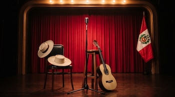 Un escenario con telón rojo, un micrófono de pie, una guitarra junto a un taburete, una silla con dos sombreros y la bandera de Perú.