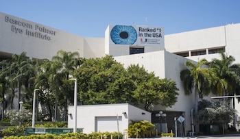 Fachada de un edificio blanco con palmeras, arbustos verdes y un cartel azul y blanco que muestra un ojo y el texto 'Ranked #1 in the USA'