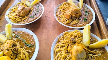 Cuatro platos de sopa seca de Chincha sobre una mesa de madera. Cada plato contiene fideos spaghetti, pollo, una salsa oscura y trozos de yuca hervida.