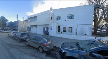 Edificio blanco de dos pisos con rejas de seguridad y varios automóviles estacionados en la calle junto a la acera