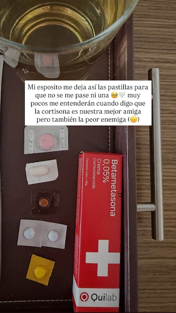 Una bandeja de madera sostiene un vaso con líquido, varios blísteres con pastillas y una caja roja de crema de betametasona
