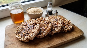 Vista aérea de varias palanquetas de arroz inflado con glaseado sobre una tabla de madera. Al fondo, un frasco de miel, un cuenco de arroz crudo y saleros.