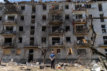 Un hombre de espaldas contempla un edificio de ladrillos dañado con ventanas destruidas, balcones rotos y restos acumulados en el suelo
