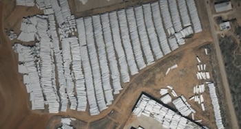 Vista aérea de un vasto campo abierto con miles de palas blancas de turbinas eólicas apiladas en largas filas y grupos. Se observan caminos de tierra