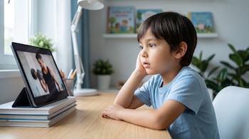 Un niño sentado frente a un escritorio, con una tablet que muestra a un hombre levantando pesas. Detrás del niño hay una ventana, una lámpara y libros en un estante.