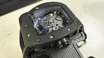 Primer plano de un reloj de pulsera negro con engranajes visibles, tornillos en el bisel y las inscripciones Richard Mille y Swiss Made.