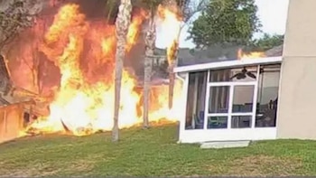 Vista de un incendio masivo con grandes llamas naranjas y humo al lado de una estructura residencial blanca con un porche cerrado