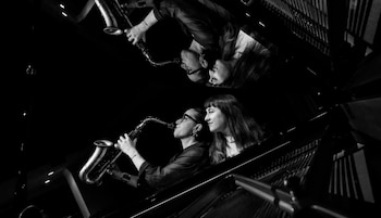 Imagen en blanco y negro de dos mujeres; una toca el saxofón, la otra mira. Reflejo invertido de ambas en la parte superior