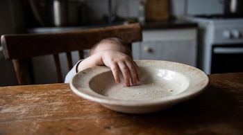 Mano de niño, plato hondo con migajas, mesa de madera, fondo borroso de cocina.